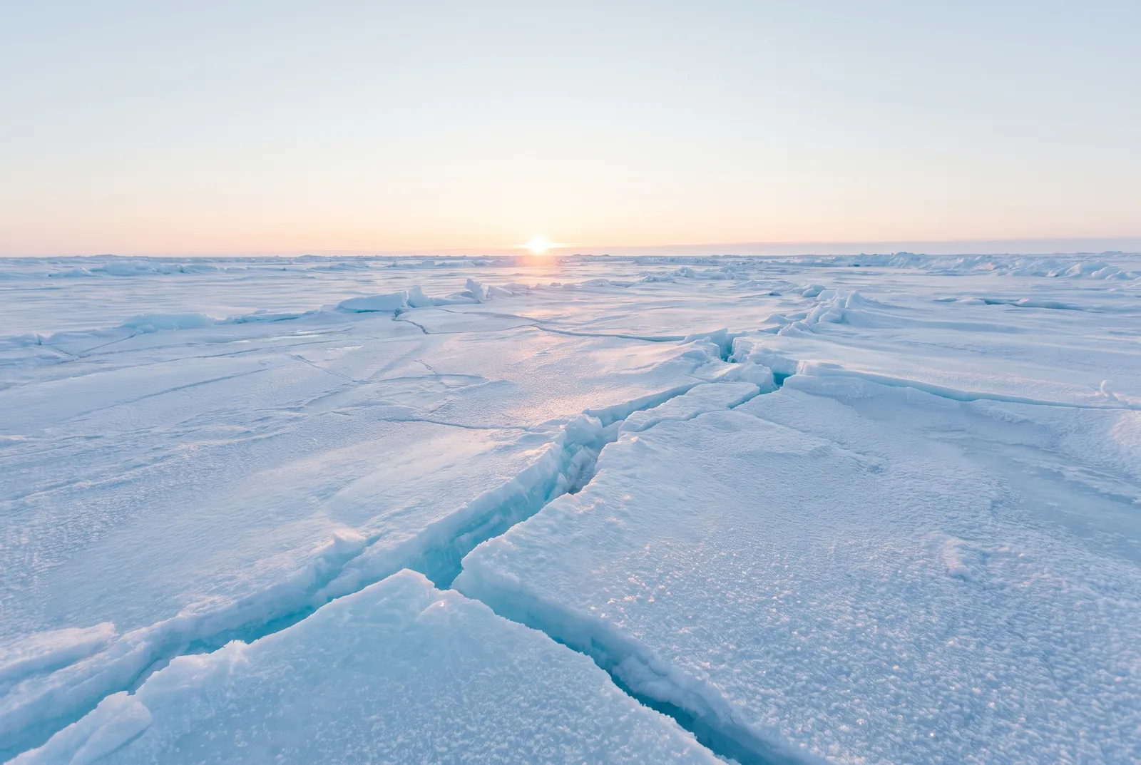 Banquise blanche et bleue traversée par une longue faille, un soleil bas sur l’horizon.
